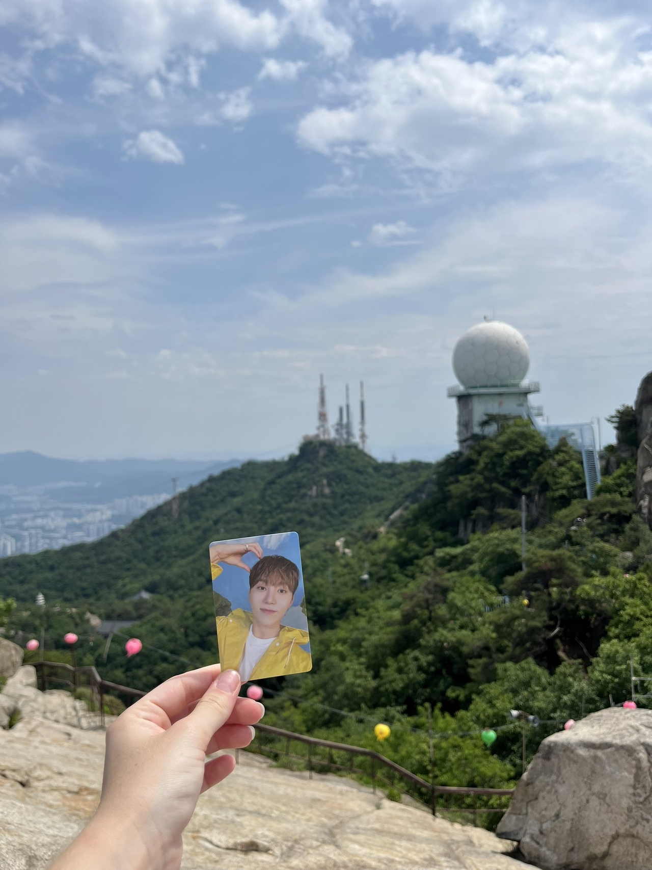 Lari, a traveler from France, takes a photo with a photocard of K-pop singer Boo Seung-kwan at the summit of Gwanaksan in Seoul in June, inspired by a 2024 video of the singer at the same location. (Lari)