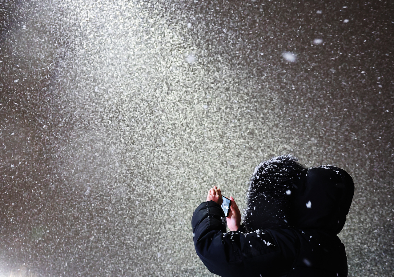 A citizen takes a photo of the snowfall in Suwon, Gyeonggi Province, as the city sees its first snowfall of the season on Thursday. (Yonhap)